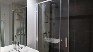 Un baño moderno con ducha de vidrio, lavamanos blanco y espejo.