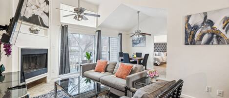A spacious living room with a fireplace, a dining area, and a bedroom with a tufted headboard.