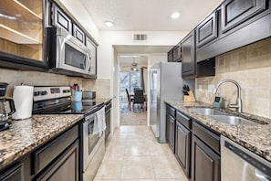 A modern kitchen with granite countertops, stainless steel appliances, and dark cabinetry.