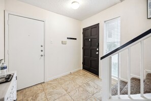 A hallway with a white door, a dark door, and a staircase with a white railing.