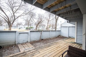 A covered outdoor deck area with a wooden floor, a small tree, and a metal gate. - i655 - Apt|Yard|9mi to Fair Park|Sleeps 4 (Irving)