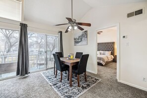A room with a dining table, chairs, a ceiling fan, a bed, and a view through a window. - i655 - Apt|Yard|9mi to Fair Park|Sleeps 4 (Irving)