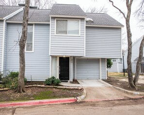 A two-story residential building with a garage, a front door, and a small front yard with a tree and shrubs. - i655 - Apt|Yard|9mi to Fair Park|Sleeps 4 (Irving)