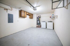 A utility room with a water heater, a washing machine, and a metal shelf with containers.