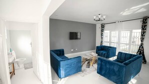 Un salon moderne avec un mur d’accent gris, un téléviseur à écran plat et des canapés en velours bleu.