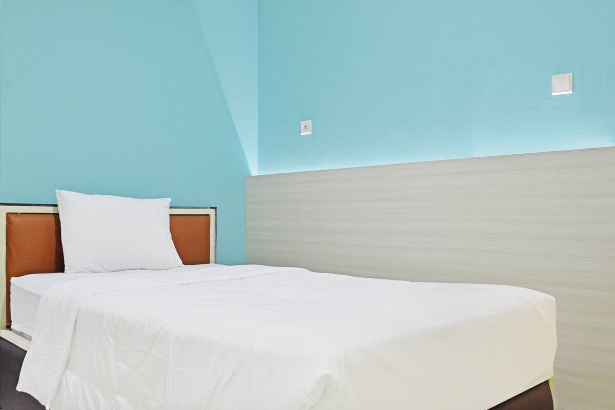 Una habitación de hotel con una cama, un cabecero y una pared azul claro.