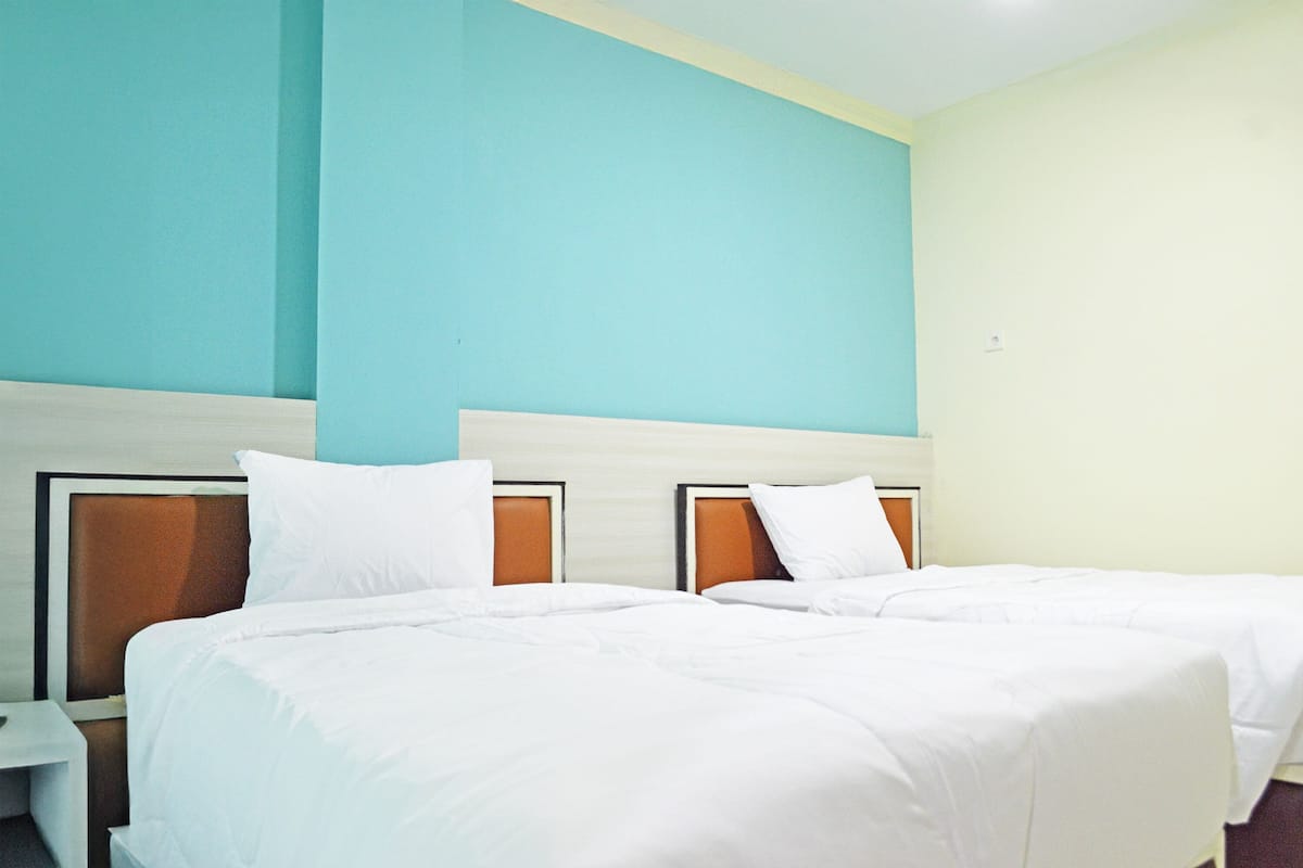 Una habitación de hotel con dos camas, una mesita de noche y una pared de color claro.