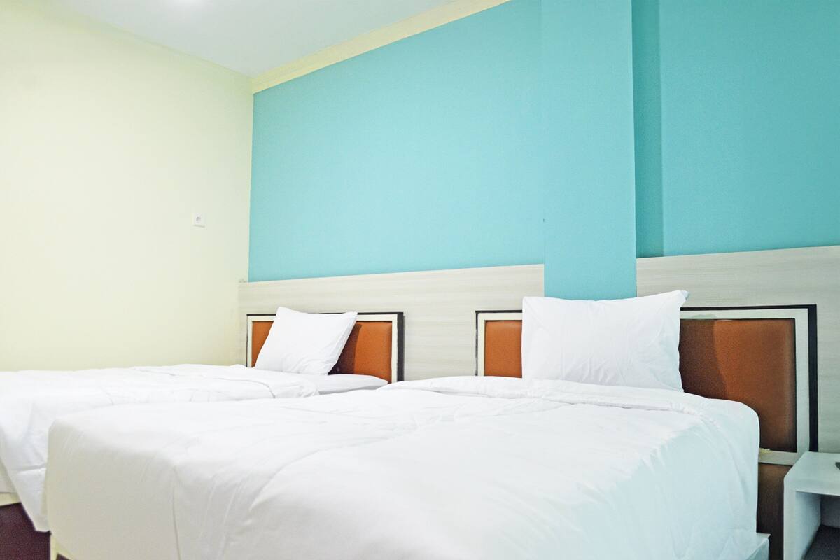 Una habitación de hotel con dos camas, cabecera de madera, ropa de cama blanca y una pared de acento color turquesa.