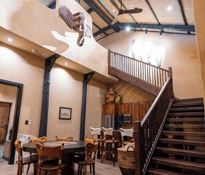 A spacious dining area with a high ceiling, rustic wooden staircase, and a mounted animal head.