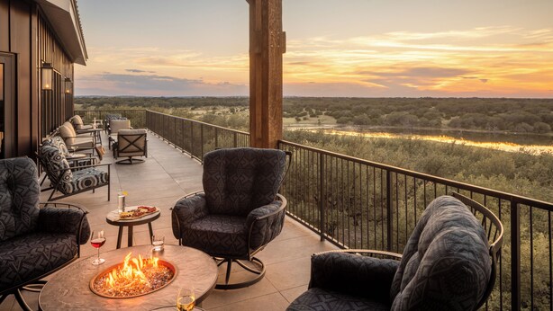 A balcony with outdoor seating, a fire pit, and a view of a river and forest.
