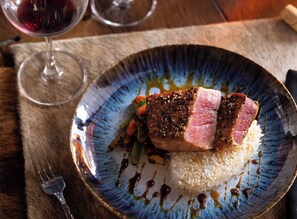 A plate with a piece of meat, rice, and vegetables, accompanied by a glass of red wine.
