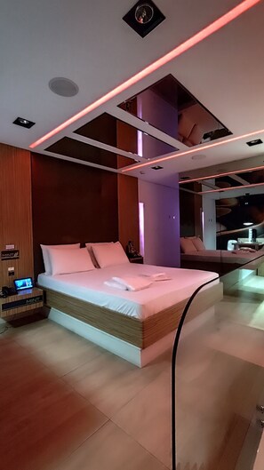 A modern bedroom with a large bed, a bedside table with a phone, and a nightstand. - Mint Motel (Guarulhos)