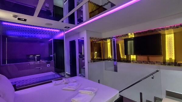 A modern hotel room with a bed, a small table, a mirror, and a TV. - Mint Motel (Guarulhos)