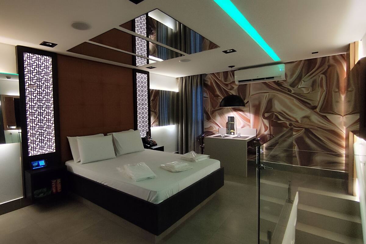 A modern hotel room with a bed, bedside table, and a large window.