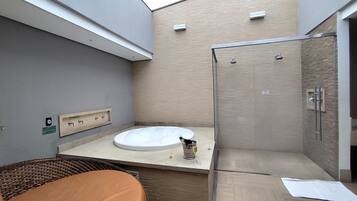 A modern bathroom with a glass-enclosed shower, a round bathtub, and a wicker chair.