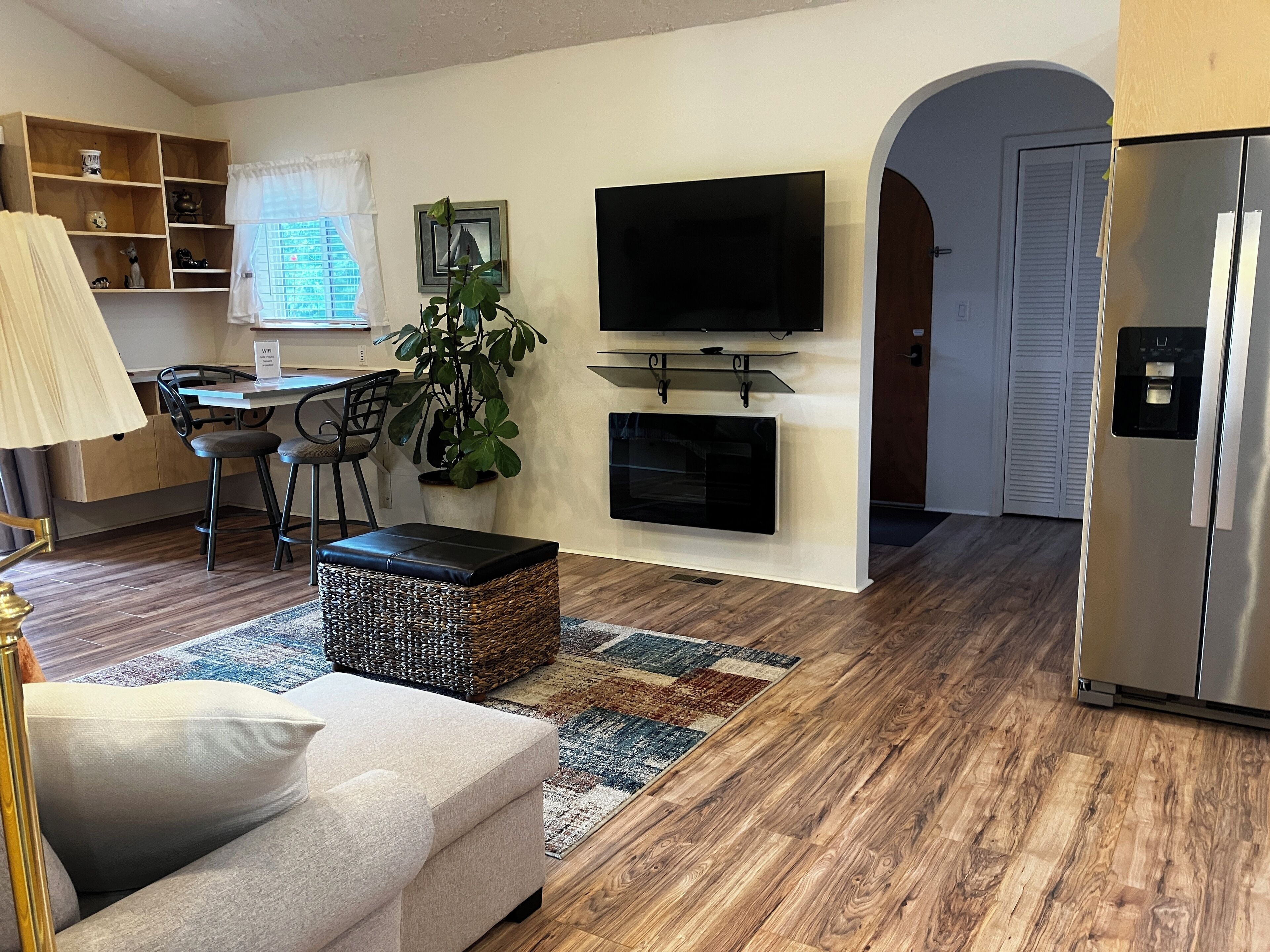 A modern living room with a sofa, a TV, a dining area with chairs, a kitchen area, and a refrigerator.