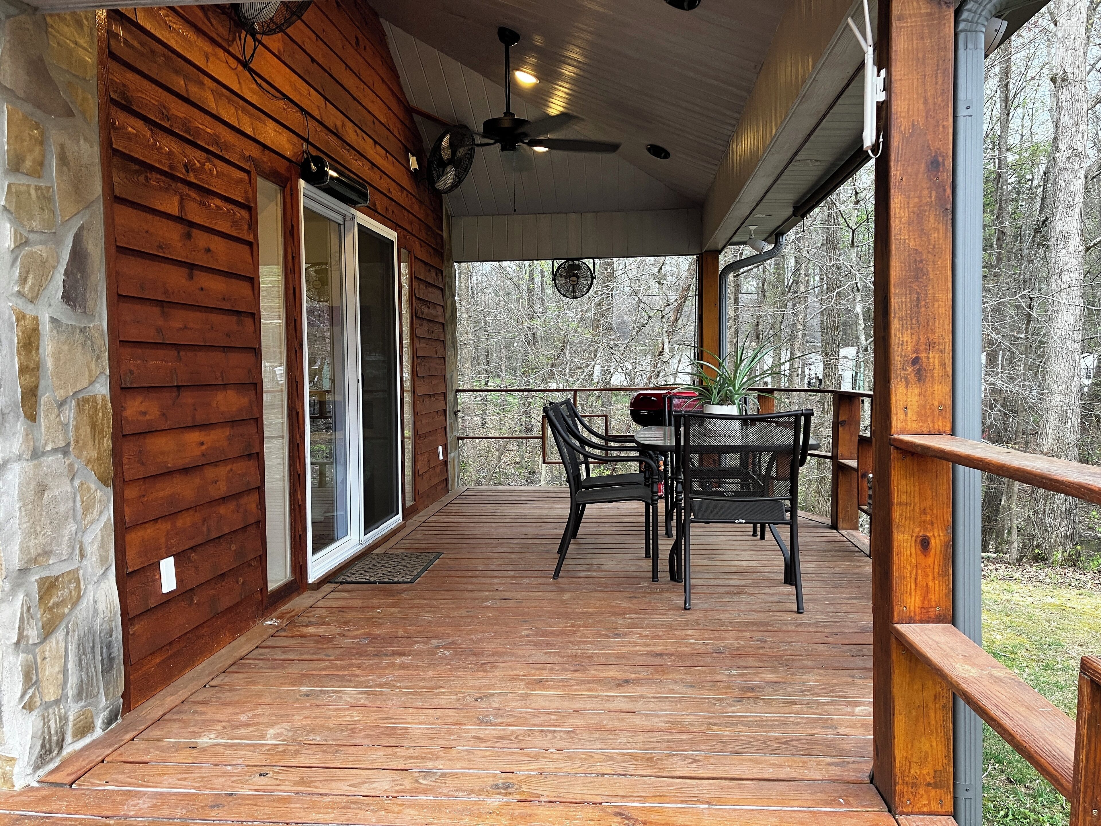 A wooden deck with a table and chairs, a ceiling fan, and a view of trees.