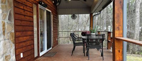 A wooden deck with a table and chairs, a ceiling fan, and a view of trees.