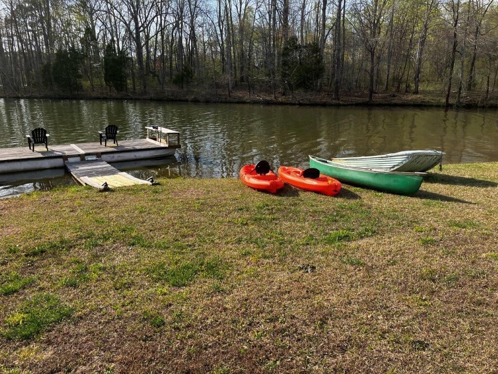 Une jetée avec des chaises et une petite table, deux kayaks et un bateau vert, le tout au bord d’un lac paisible, entouré d’arbres.