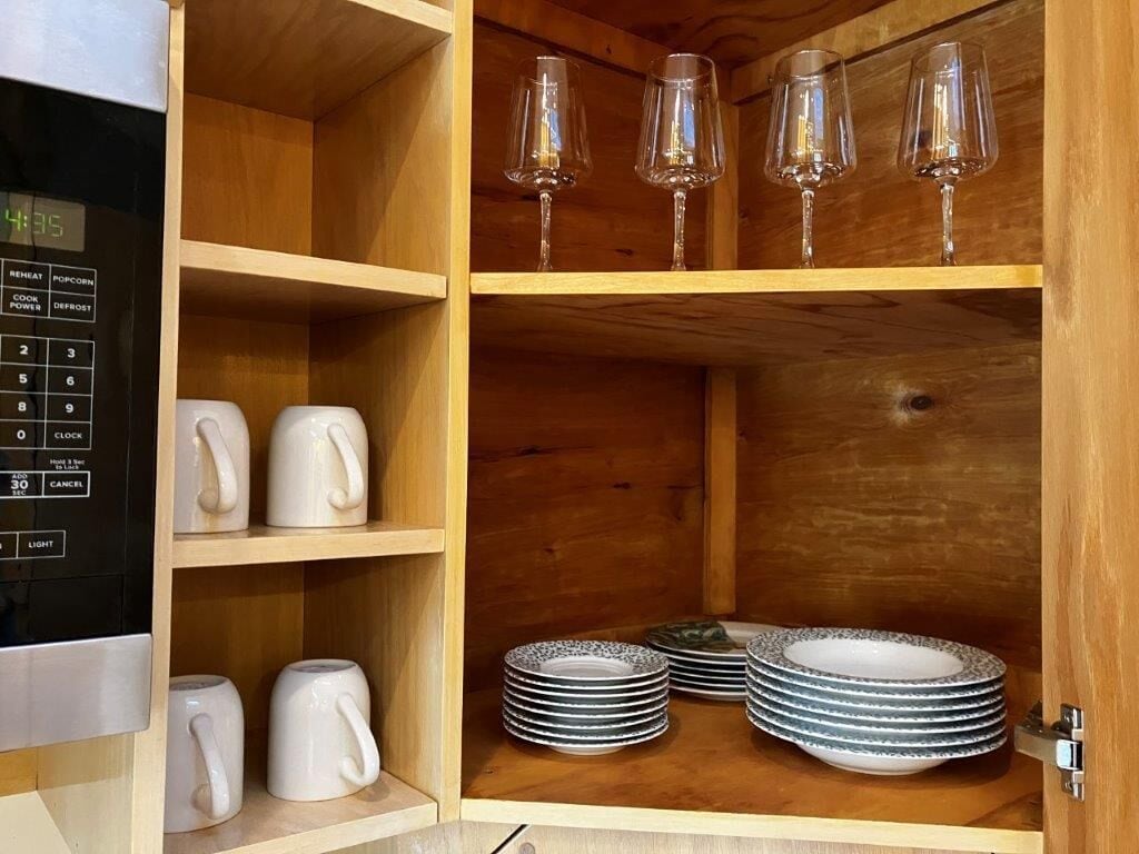 Un meuble en bois doté d’étagères où sont rangées des tasses blanches, des verres à vin transparents et des assiettes empilées.