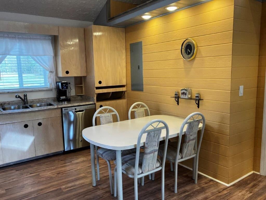 A compact kitchen with a white table and four chairs, a coffee maker, and a clock on the wall.