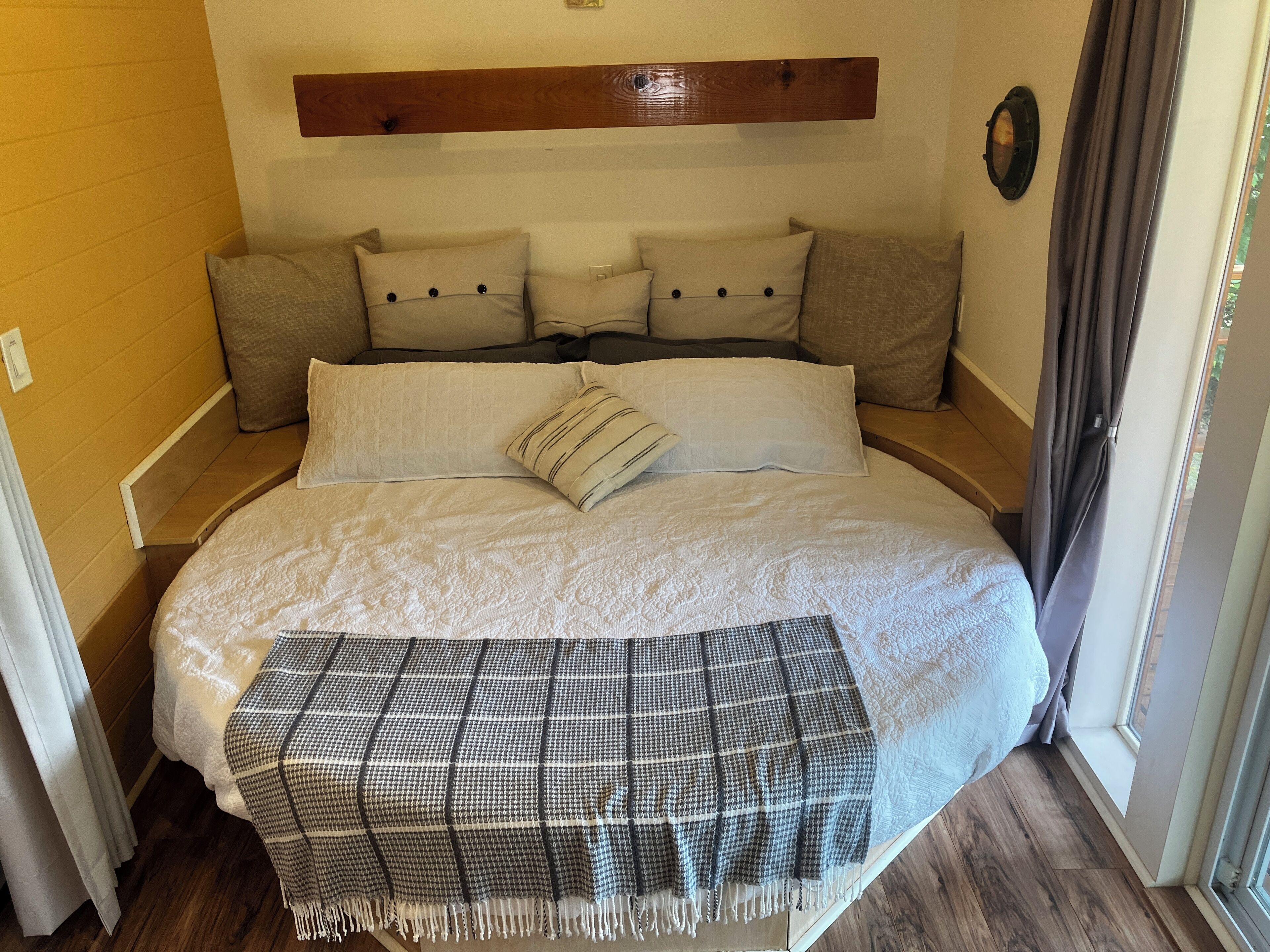 Una cama con un edredón blanco acolchado, una manta de cuadros y varias almohadas.