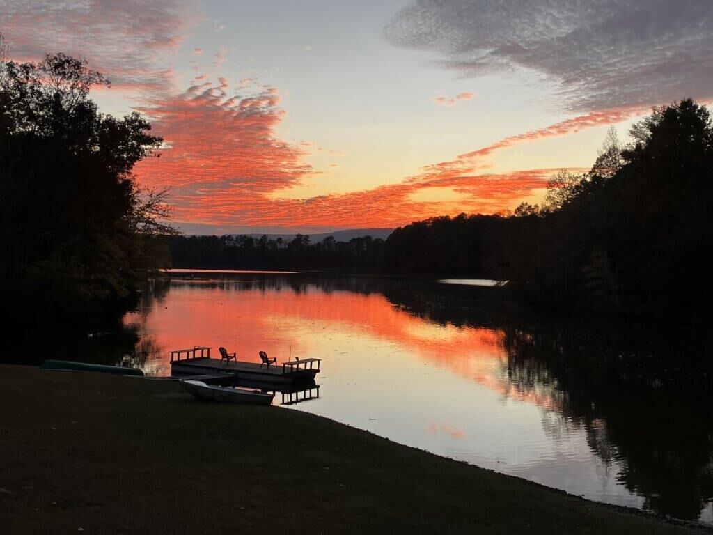 A calm lake at sunset with a dock and chairs.
