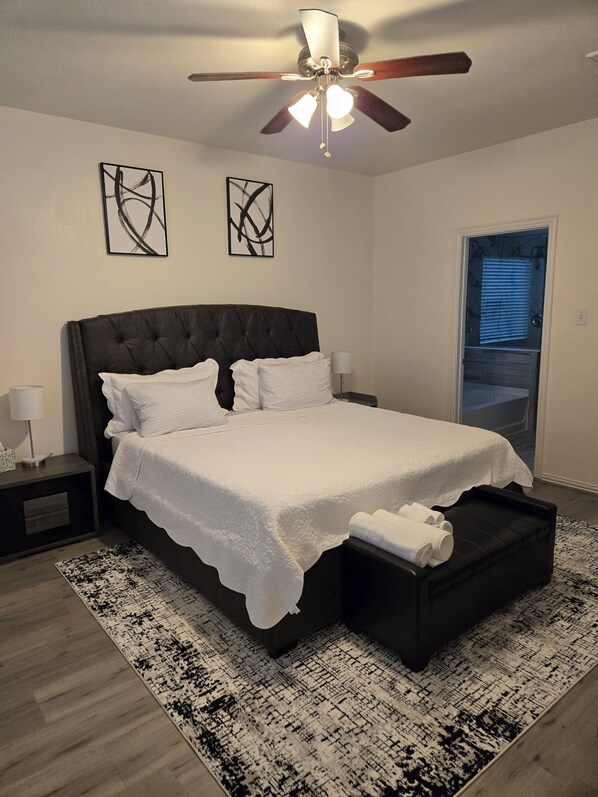 A bedroom with a large bed, a ceiling fan, and two abstract wall art pieces.