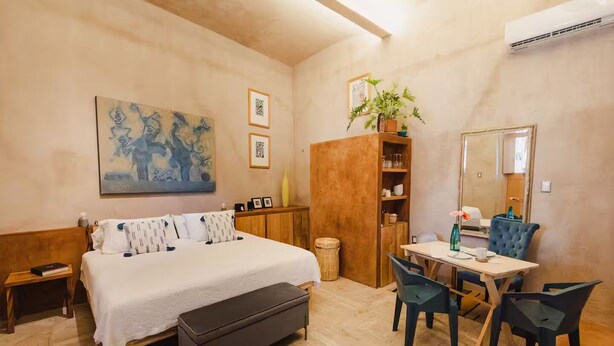 A bedroom with a bed, bedside table, bench, desk, chairs, and a mirror.