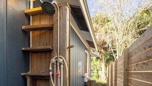 A wooden outdoor shower area with a metal frame, wooden steps, and a wooden fence.