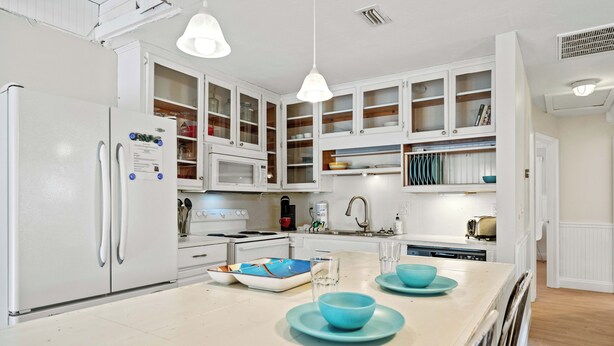 A modern kitchen with white cabinetry, a central island with blue plates, and a white refrigerator.