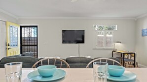 A living room with a TV, a dining table with blue plates, and a sofa.