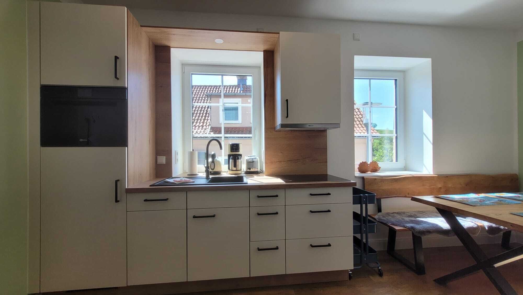 Een moderne keuken met witte kasten, een ingebouwde oven en een raam met uitzicht op een woonwijk.