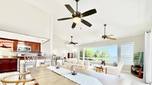 A spacious living area with a large wooden dining table, two ceiling fans, and a view of the outdoors through large windows. - Waterfront,Private home&pool,Breathtaking Views,Great Location. Enjoy paradise! (St Thomas)
