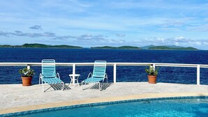 A poolside area with two blue lounge chairs and potted plants, overlooking a large body of water and distant green hills. - Waterfront,Private home&pool,Breathtaking Views,Great Location. Enjoy paradise! (St Thomas)