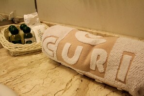 Une serviette sur laquelle on peut apercevoir le mot « GUR », un panier contenant des articles de toilette et un mur à texture.