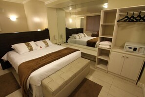 Une chambre d’hôtel avec un grand lit, une armoire, un miroir et un four à micro-ondes.