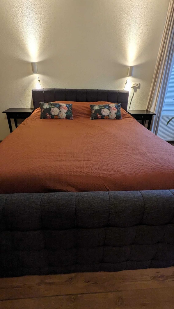 Un letto con una testiera scura e una coperta rossa, affiancato da due comodini con lampade.