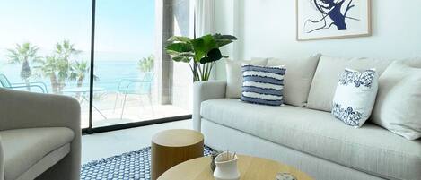 A modern living room with a sofa, a round wooden coffee table, and a view of the ocean through large windows.