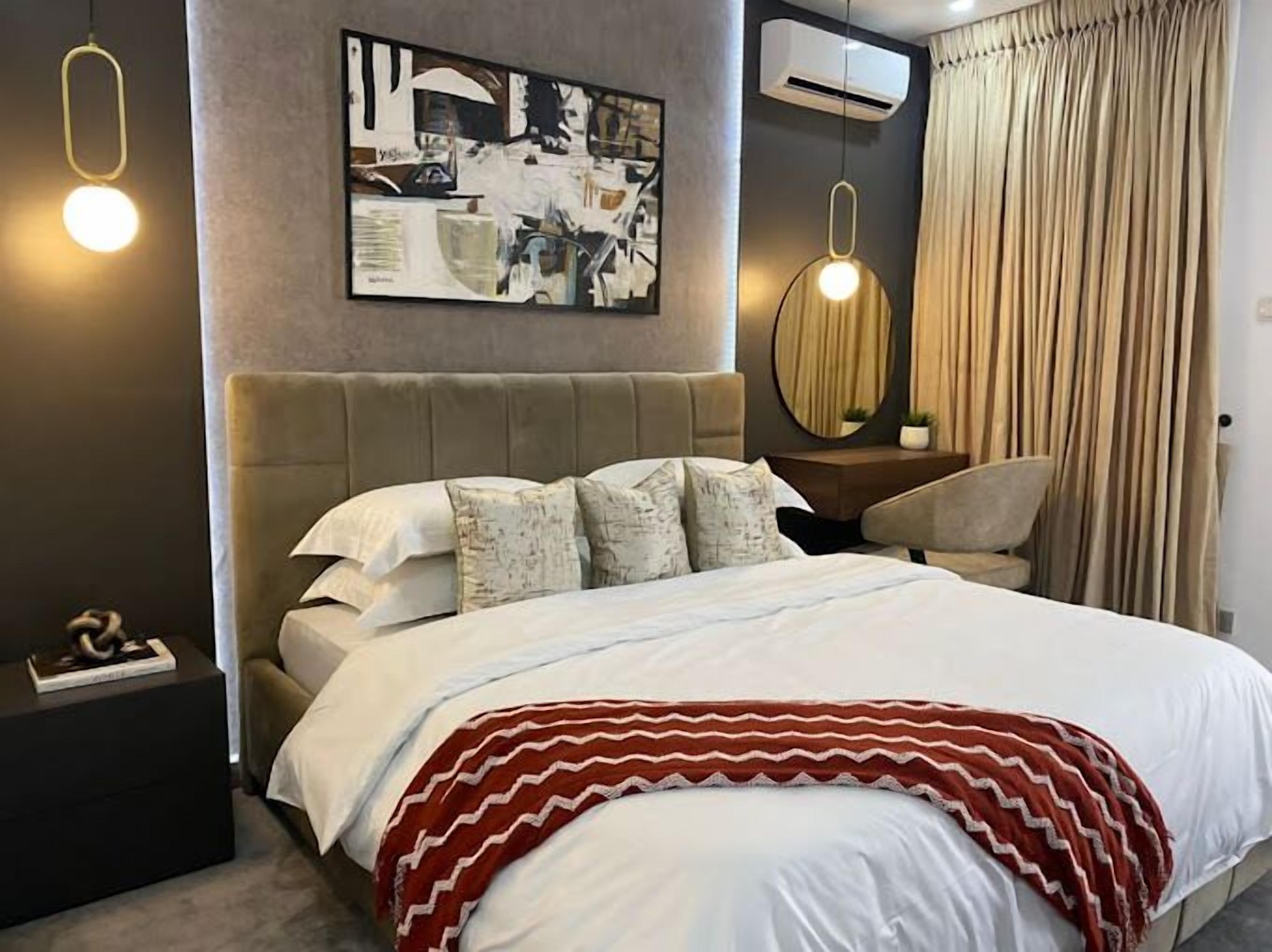 Un dormitorio moderno con una cama grande, un cabecero, un cuadro, un espejo redondo y una mesita de noche.