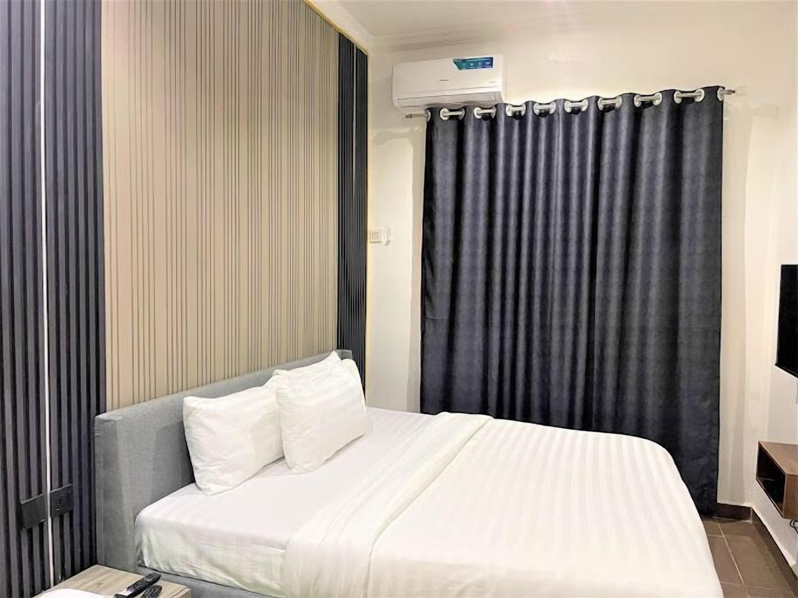 A hotel room with a bed, a TV, and an air conditioning unit.