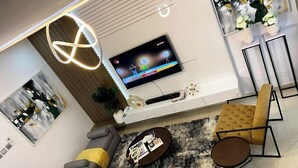 A modern living room with a sectional sofa, a yellow armchair, a coffee table, and a TV mounted on the wall. - Duke Residence (Ibadan)