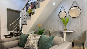 A modern living room with a grey sofa, a staircase, and a dining area. - Duke Residence (Ibadan)