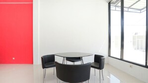 A modern room with a round table and four black chairs, large windows, and a red accent wall. - Hotel O Mojoanyar Near Terminal Bis Mojokerto (Mojokerto)