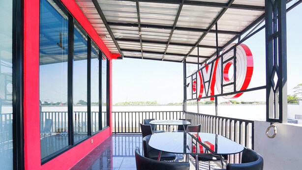 A covered outdoor seating area with tables and chairs, large windows, and a view of the water. - Hotel O Mojoanyar Near Terminal Bis Mojokerto (Mojokerto)