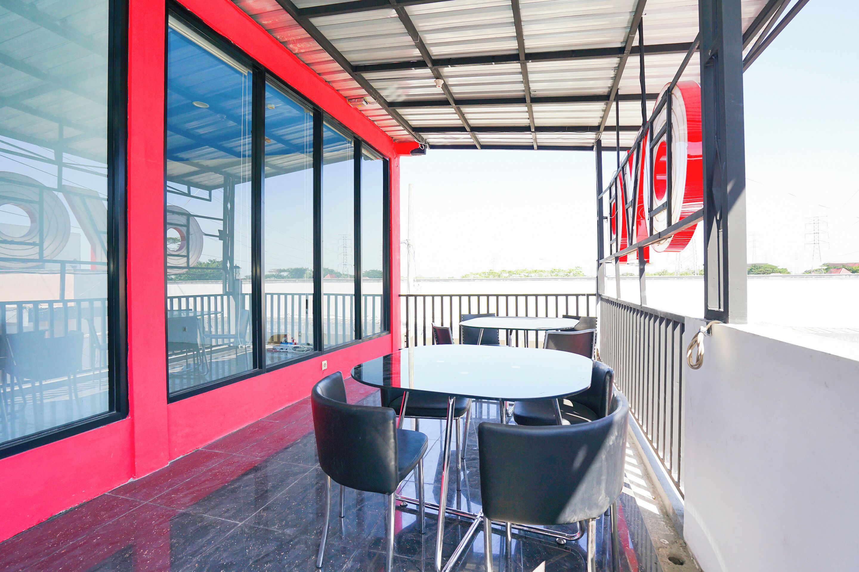 Un espacio de estar al aire libre cubierto, con una mesa, sillas, ventanas grandes y una pared roja.