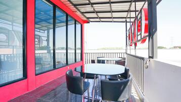 Un espacio de estar al aire libre cubierto, con una mesa, sillas, ventanas grandes y una pared roja.