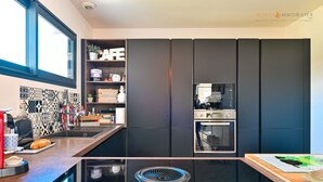 A modern kitchen with a black induction cooktop, a built-in oven, and a coffee machine. - AIR-CONDITIONED VILLA WITH POOL IN PORTICCIO (Grosseto-Prugna)