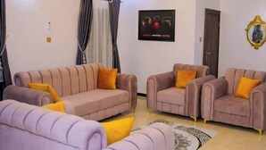 A living room with two sofas, a coffee table, and a chandelier. - D.T Homes Luxury Apartment (Ibadan)