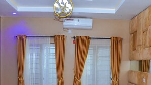 A hotel room with a bed, curtains, an air conditioning unit, and a ceiling light fixture. - D.T Homes Luxury Apartment (Ibadan)